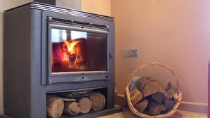 Un poêle à bois avec une réserve de bûches en dessous et un panier de bois de chauffage sur la droite.