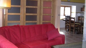 Un canapé rouge dans une pièce avec des poutres en bois, une porte avec des panneaux de verre et un coin repas avec des chaises.