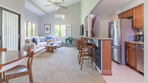 A spacious living area with a dining table, chairs, a sofa, and a kitchen area with a refrigerator and cabinets.