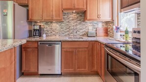 A modern kitchen with wooden cabinets, a stainless steel dishwasher, a tiled backsplash, and a built-in oven.