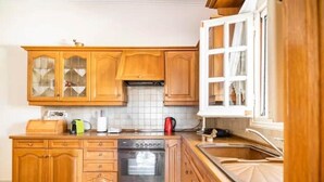A kitchen with wooden cabinets, a built-in oven, a sink, and a window with curtains. - Apartment 'Villa Dorita' with Sea View, Wi-Fi and Air Conditioning (Corfu)