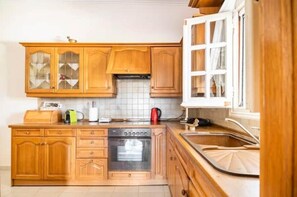 Una cucina con mobili in legno, forno a incasso, lavello e finestra con tende.