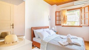 A bedroom with a wooden ceiling, a bed with white bedding, a window with curtains, and a hat on a table. - Apartment 'Villa Dorita' with Sea View, Wi-Fi and Air Conditioning (Corfu)