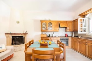 Uma cozinha acolhedora com armários de madeira, uma mesa de jantar posta para dois e uma lareira.