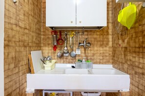 Une cuisine avec un évier blanc, des ustensiles suspendus et une passoire jaune.
