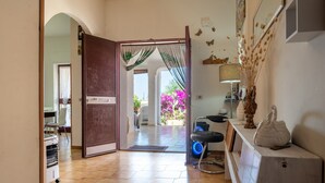 An open door leading to a bright room with a tiled floor, a desk with a chair, a lamp, and a decorative vase.