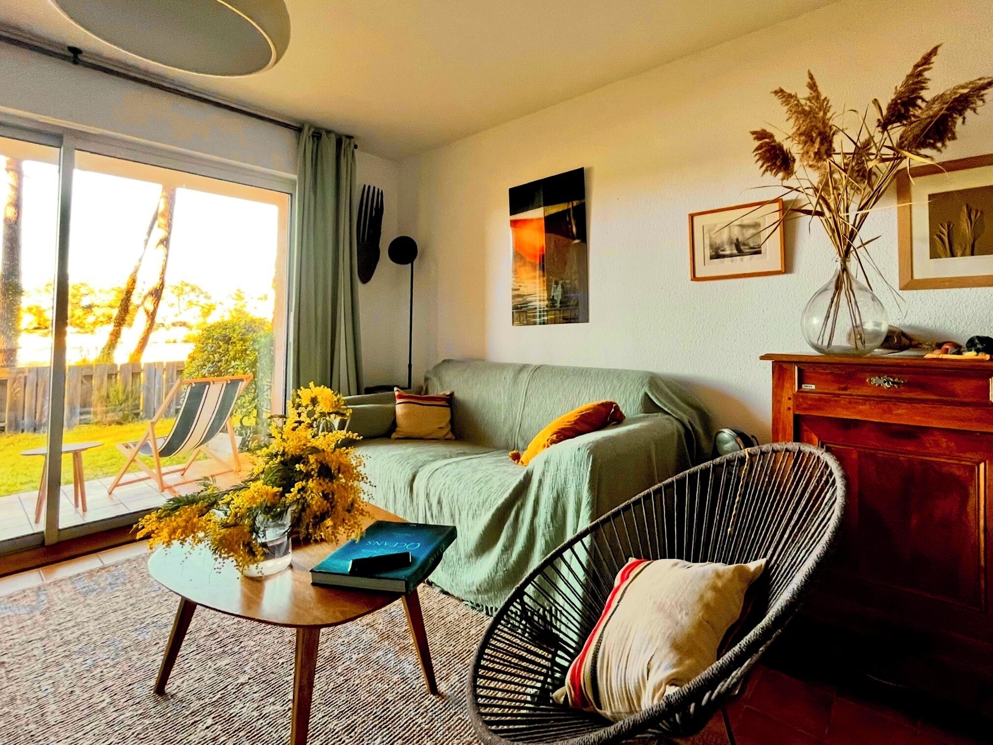 A living room with a sofa, a chair, a table with a book, and a vase with flowers.