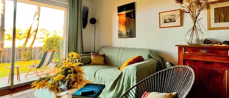 Un salon avec un canapé, un fauteuil, une table sur laquelle se trouve un livre et un vase rempli de fleurs.