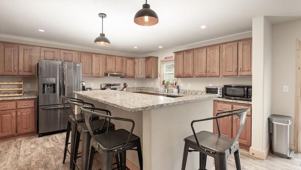 A modern kitchen with wooden cabinets, stainless steel appliances, a granite island, and bar stools. - 635 Wapiti, Hot tub, on FREE shuttle route (Fraser)