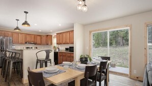 A modern kitchen with wooden cabinets, a dining area with a table set for six, and a large sliding glass door leading to a deck. - 635 Wapiti, Hot tub, on FREE shuttle route (Fraser)