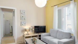 En stue med sofa, sofabord med blomster, fjernsyn og lampe.