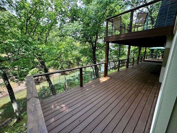 A wooden deck with a railing overlooking a river, surrounded by trees.