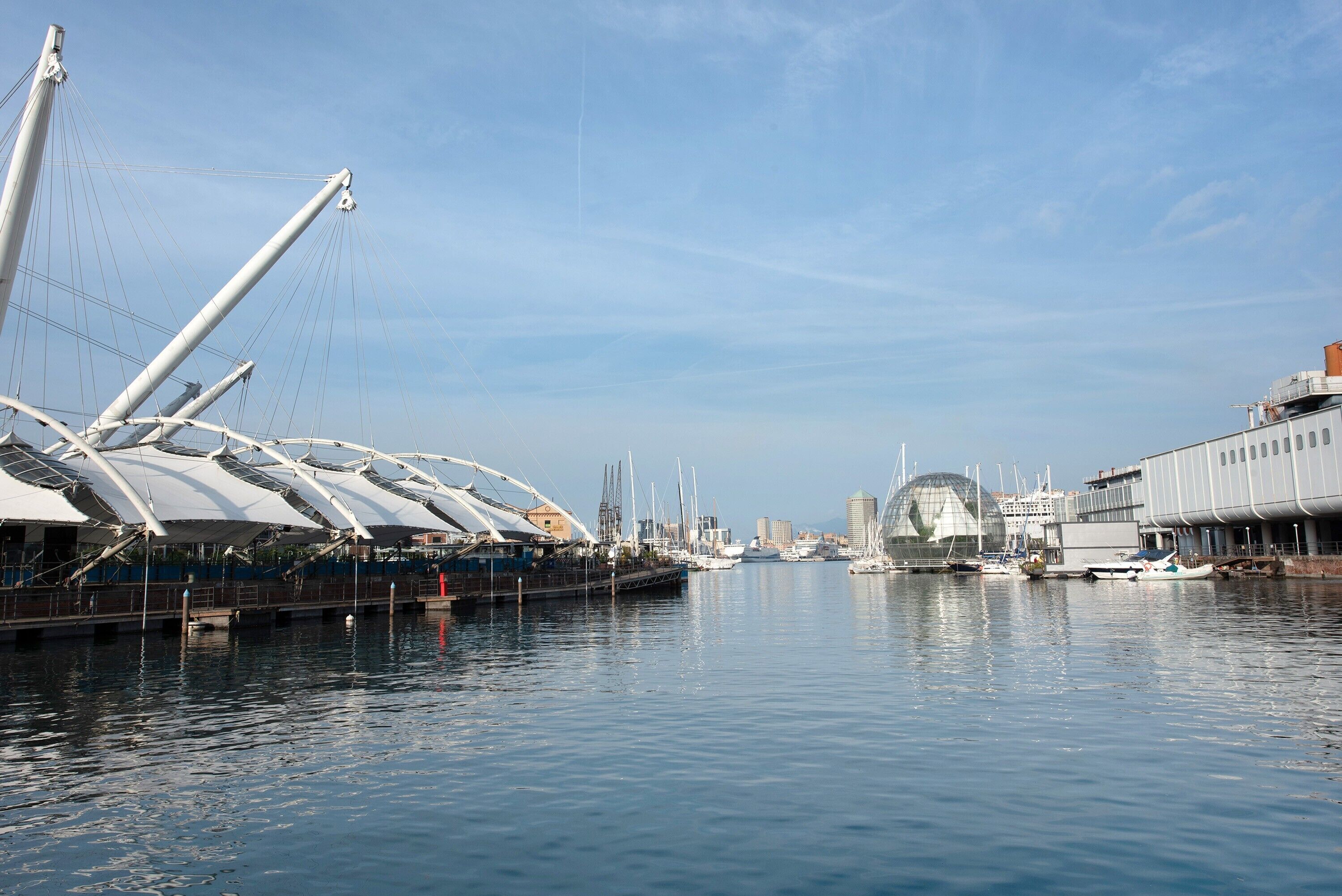 A marina with boats, a large sailboat, and a modern building with a dome.