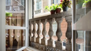Une fenêtre donnant sur la façade d’un immeuble, une rambarde de balcon et des plantes en pot.