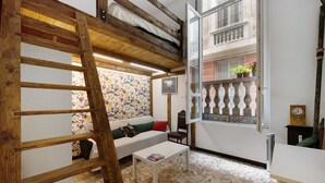 Une pièce avec une échelle en bois, un canapé blanc, une petite table, un sol carrelé et un balcon agrémenté de plantes.