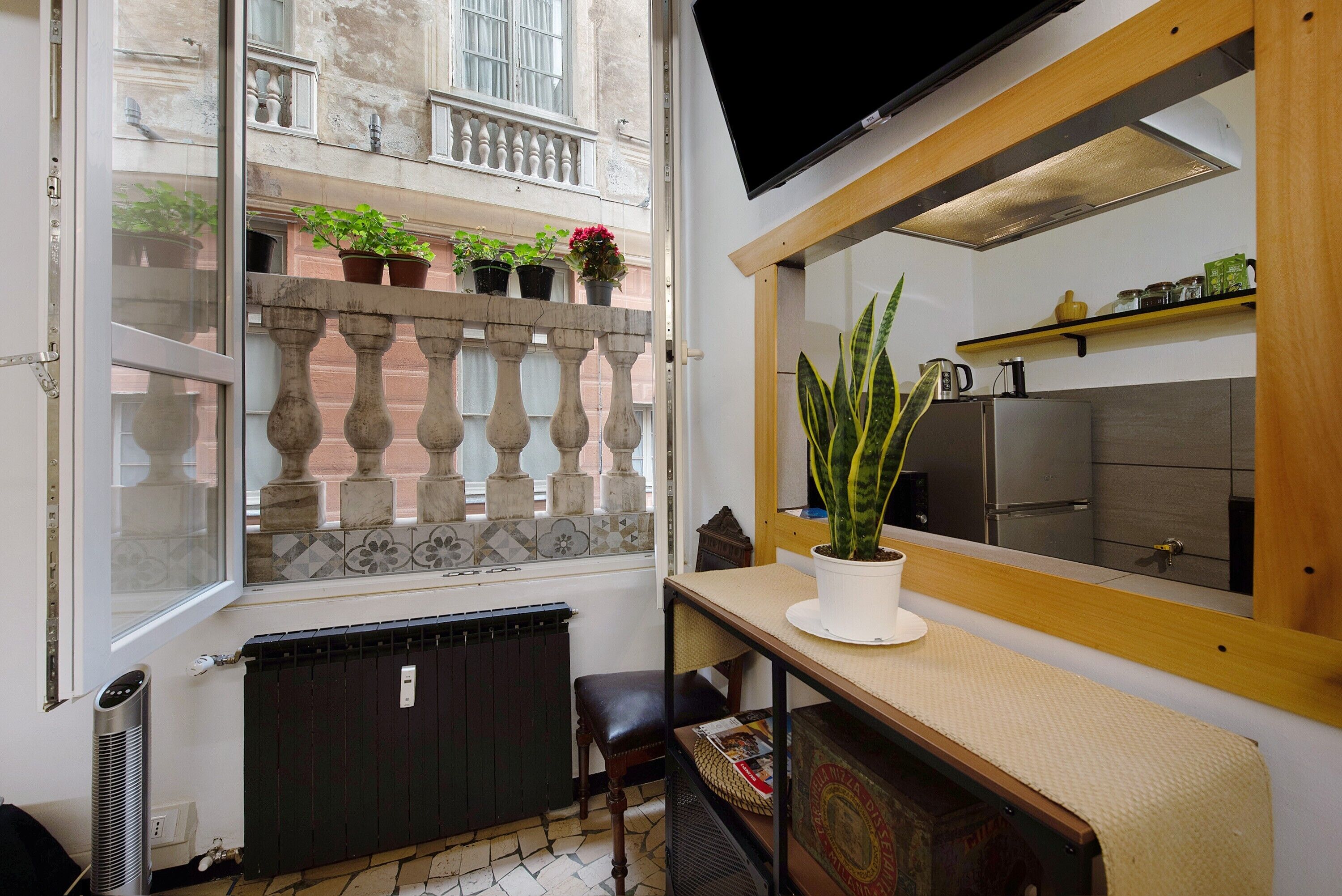 A small kitchen with a refrigerator, a potted plant, and a window overlooking a balcony with potted plants.