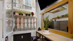 Une petite cuisine équipée d’un réfrigérateur, agrémentée d’une plante en pot et dotée d’une fenêtre donnant sur un balcon également orné de plantes en pot.