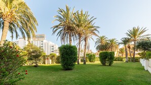 A well-maintained garden with palm trees and a building in the background. - Apartment 'Las Buganvillas' with Shared Pool, Private Terrace and Air Conditioning (Roquetas de Mar)