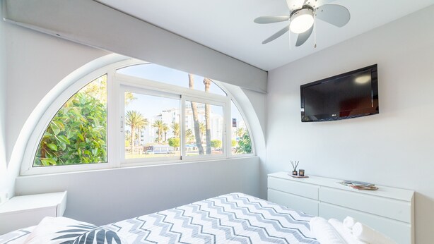 A bedroom with a bed, a TV, a window, and a ceiling fan. - Apartment 'Las Buganvillas' with Shared Pool, Private Terrace and Air Conditioning (Roquetas de Mar)