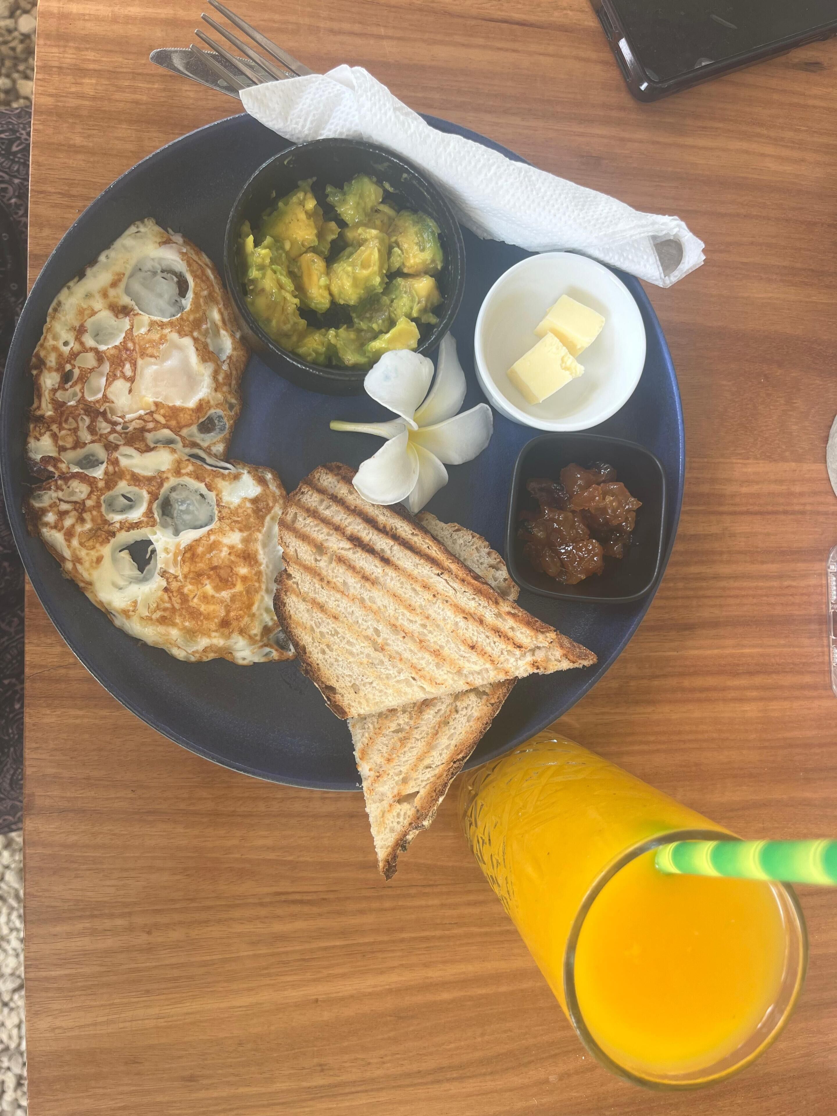 A breakfast plate with pancakes, toast, a fruit bowl, a butter dish, and a glass of orange juice.