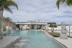 A swimming pool with a waterfall feature, a statue, and a building with solar panels.