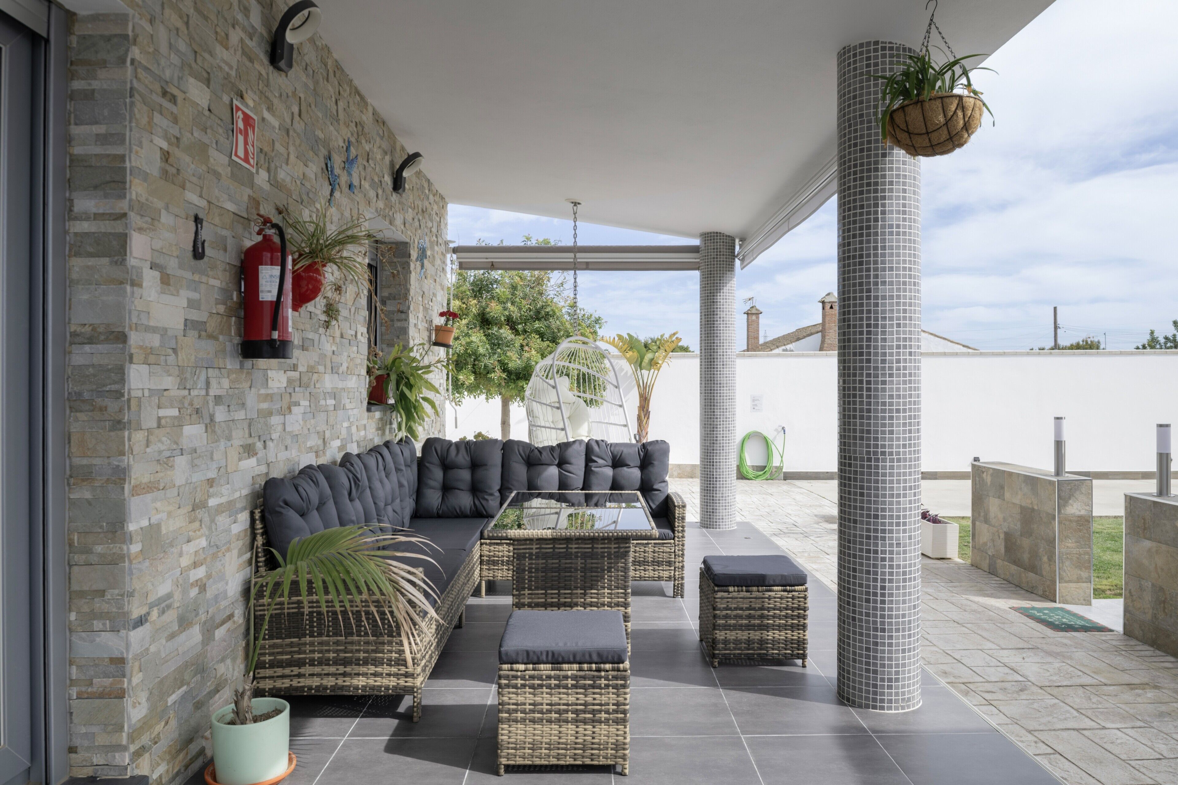 Un'area relax esterna coperta, con divano componibile, mobili in vimini e piante in vaso.