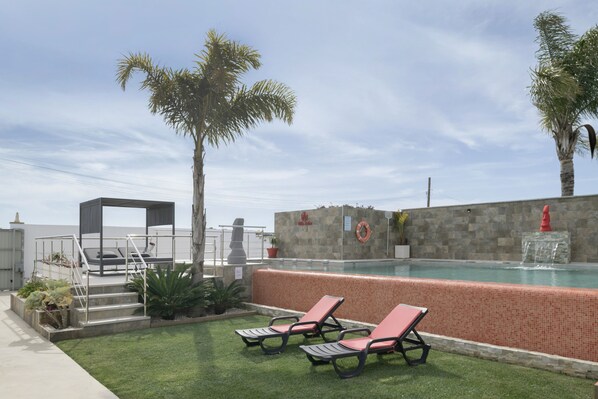 A pool area with lounge chairs, a covered seating area, and a stone wall with a lifebuoy.