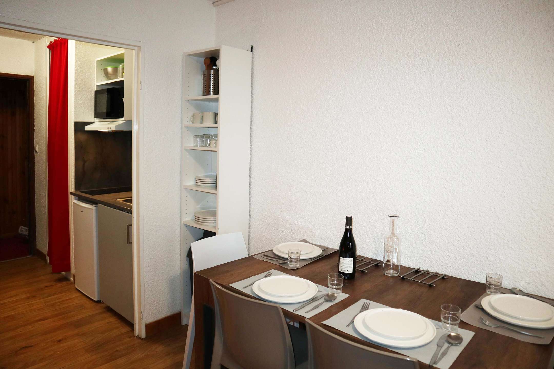 Un comedor con una mesa preparada para cuatro personas, una botella de vino y un microondas al fondo.