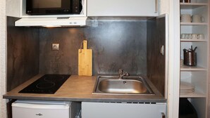 A compact kitchen with a microwave, a sink, a small refrigerator, and a wooden cutting board.