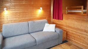 A grey sofa with a white pillow in a wooden room with two wall-mounted lights.