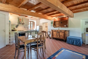 A spacious kitchen with wooden beams, a dining area with a table and chairs, and a blue rug on the floor.