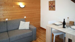 Une pièce chaleureuse avec un canapé gris, un mur en bois, une table à manger avec des chaises et un luminaire fixé au mur.