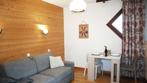 Une pièce chaleureuse avec un canapé gris, des murs en bois, une table à manger avec des chaises et un rideau à motifs.