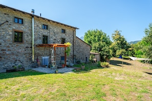 Un bâtiment en pierre doté d’un patio couvert, d’un petit abri de jardin et d’une cour gazonnée.