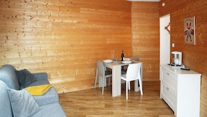Una stanza accogliente con una parete in legno, un tavolo da pranzo con sedie, una cassettiera bianca e un divano grigio con cuscini.