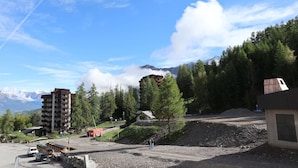 Zona montuosa con un edificio a più piani, un parcheggio e una strada sterrata.