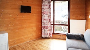 Una stanza con pareti in legno, un divano grigio, un armadietto bianco e una finestra con tende a motivi.