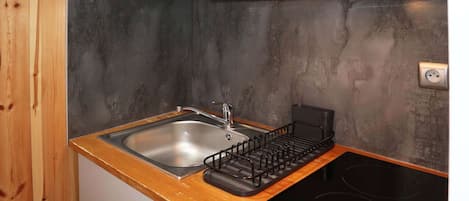 A compact kitchen with a wooden countertop, a stainless steel sink, and a black induction cooktop.