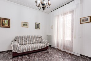 A room with a sofa, a radiator, a chandelier, and framed pictures on the wall.