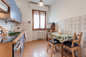 A compact kitchen with a dining area, featuring a window, a radiator, and a tiled backsplash.
