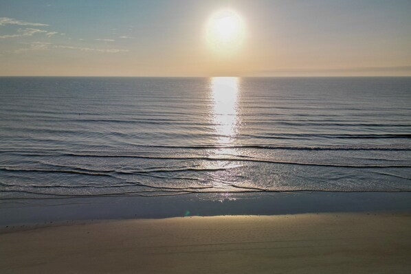 A beach with waves and the sun reflecting on the water.