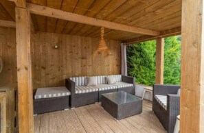 A covered outdoor seating area with wicker furniture, a glass table, and a hanging light fixture.