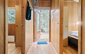 A narrow wooden hallway with a bed on the right and a window at the end.
