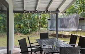 An outdoor patio with a wooden table and chairs, a swing set, and a trampoline.