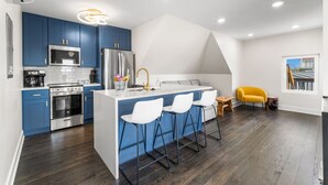 Une cuisine moderne avec des meubles bleus, un îlot central doté de tabourets de bar, des appareils en acier inoxydable et un luminaire suspendu lumineux.
