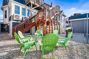 Een meerlaags gebouw met een houten trap naar een terras, omringd door groene stoelen en een barbecue.