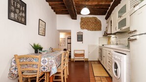 A kitchen with a washing machine, a dining table with chairs, and a brick wall. - Castellare Degli Ugurgieri Central Apt in Siena (Siena)