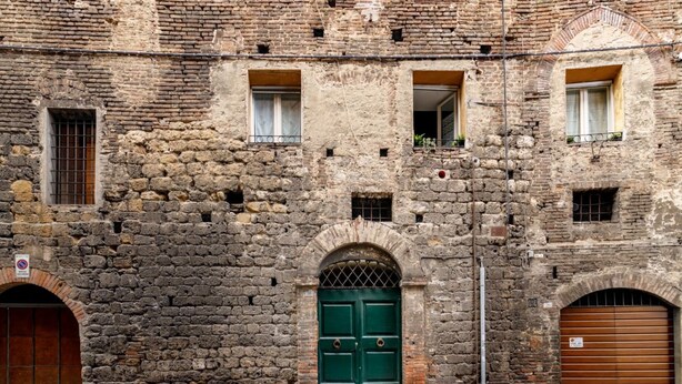 A historic stone building with a green door, arched windows, and a no parking sign. - Castellare Degli Ugurgieri Central Apt in Siena (Siena)
