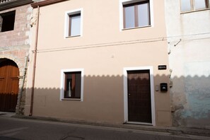 A two-story building with a beige facade, a wooden door, and a small window.