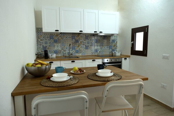 A small kitchen with white cabinets, a tiled backsplash, a wooden countertop, and two white chairs.